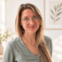 Katarzyna Mozgawa - założycielka Centrum W Pełni. Portret uśmiechniętej specjalistki Centrum W Pełni w Szczecinie, w jasnym, przytulnym wnętrzu, na tle rośliny i obrazu.