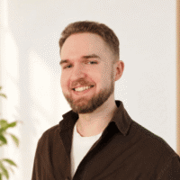 Aleksander Falkiewicz – psycholog i psychoterapeuta w trakcie szkolenia w Centrum W Pełni w Szczecinie. Uśmiechnięty, na tle jasnej ściany.